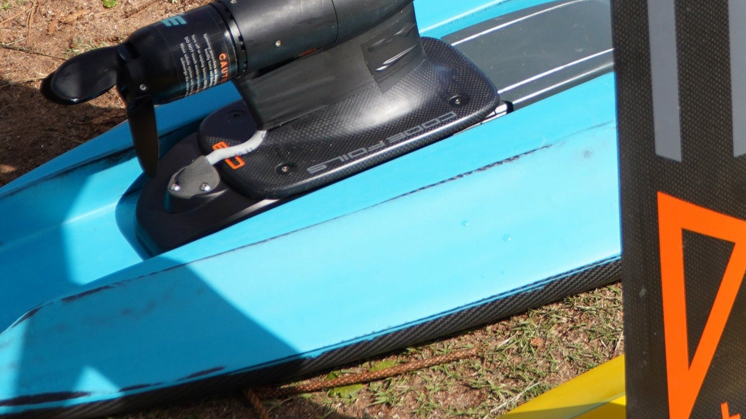 Close up shot of a Foil Drive assist kit mounted on a blue Kruzer RTS Foil Drive board by Amos Shapes on the beach