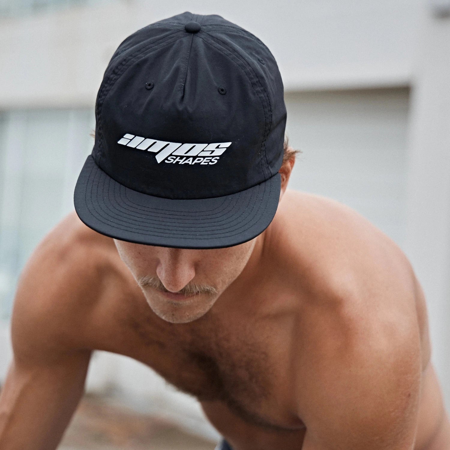 A man wearing a black Amos Shapes surf hat with the logo in white on the front