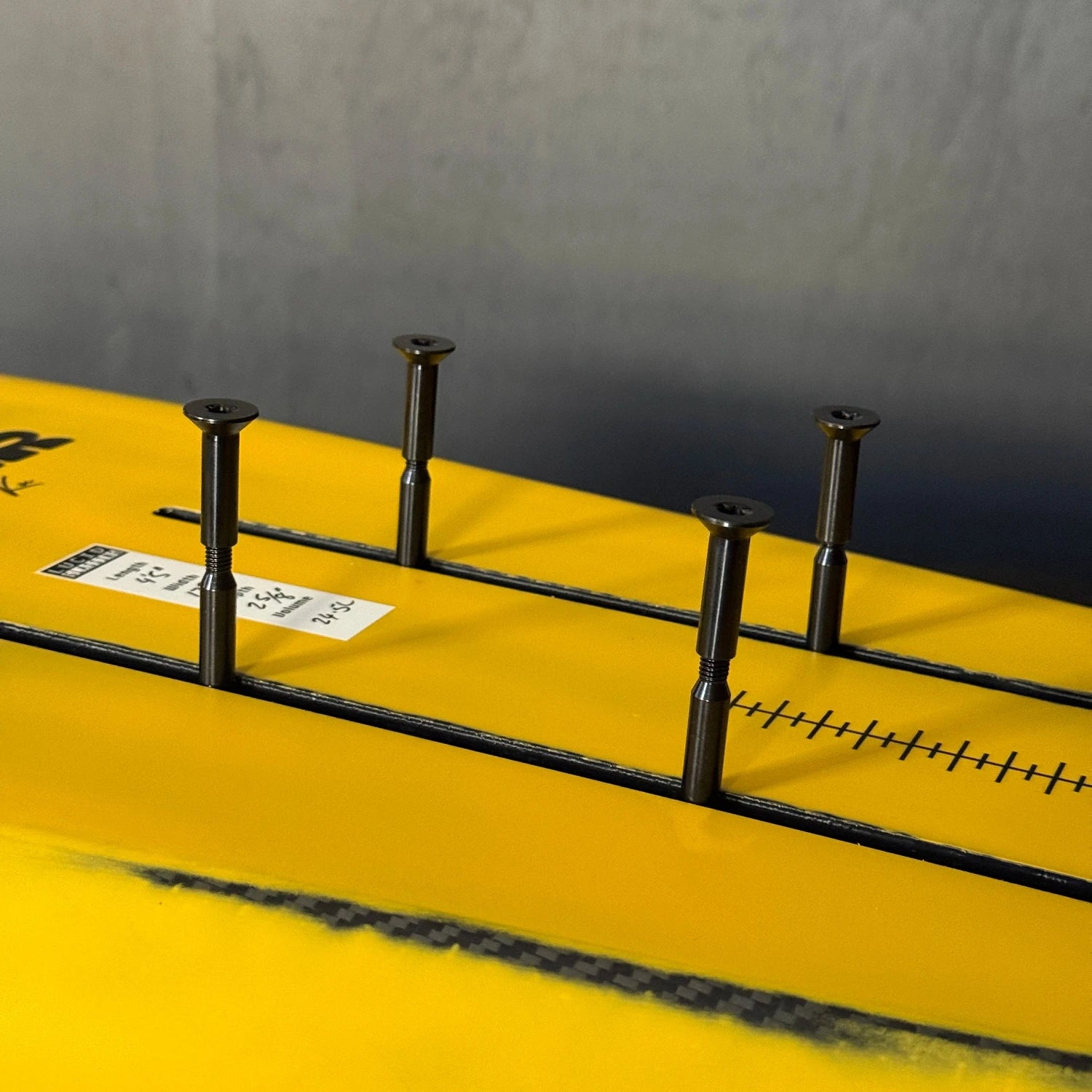 Close up shot of four Foil Drive split bolts mounted on a yellow Kruzer carbon foilboard by Amos Shapes