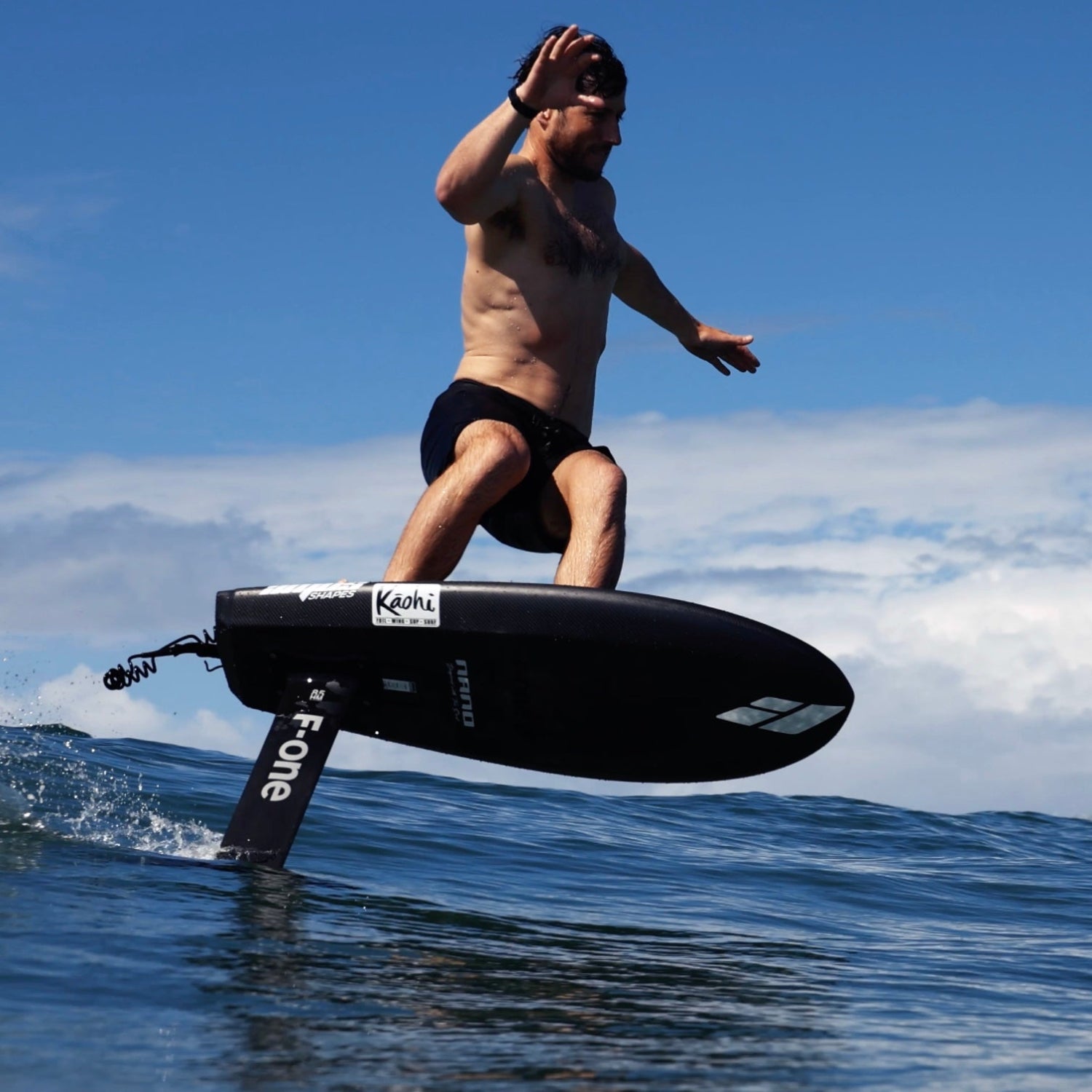 A man riding the Amos Shapes Nano Prone surf carbon foilboard in ocean conditions on a sunny day