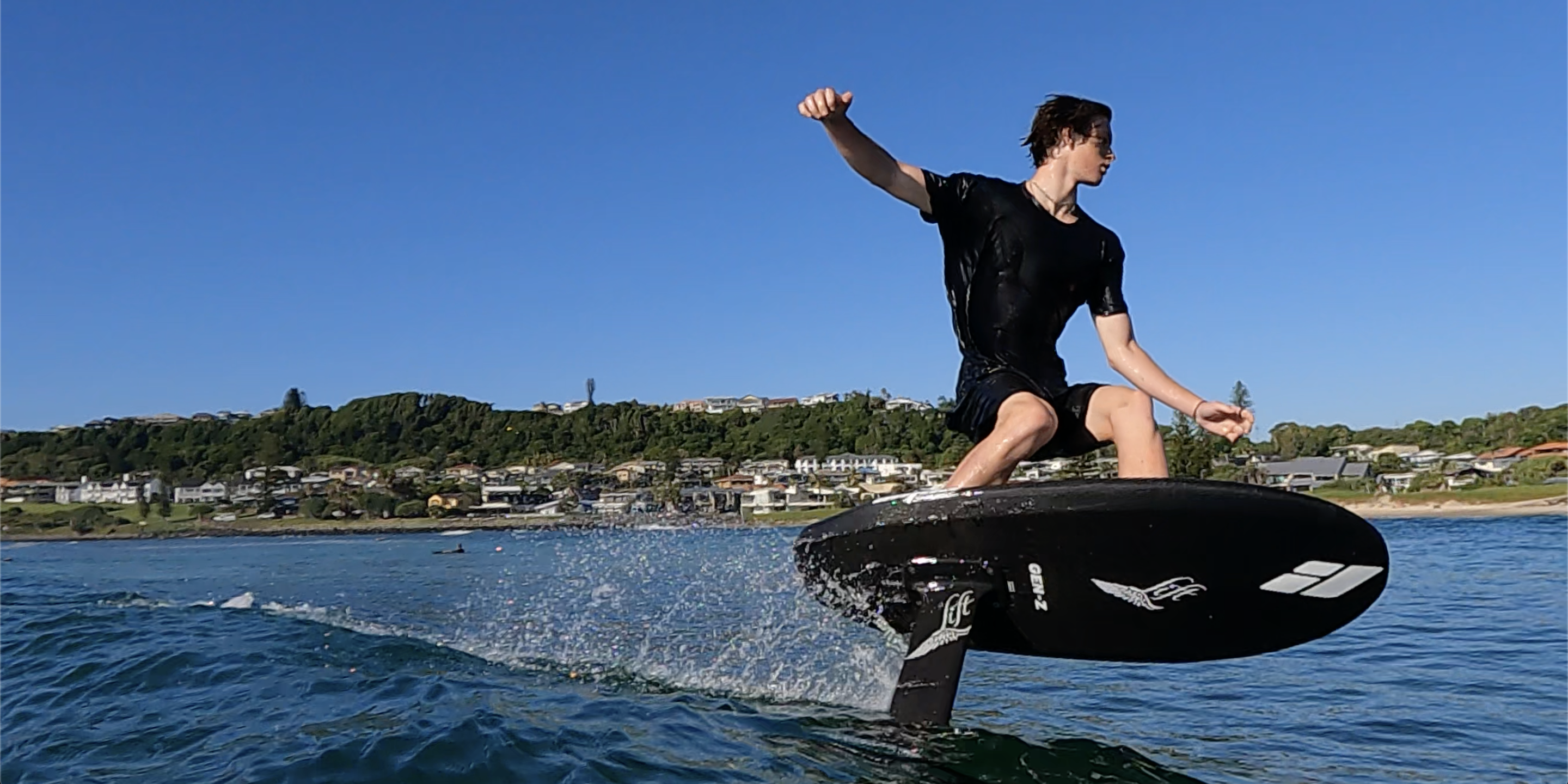A man riding a surf foilboard on an Amos Shapes Foilboard and Lift Foils hydrofoil with his arms out wide 