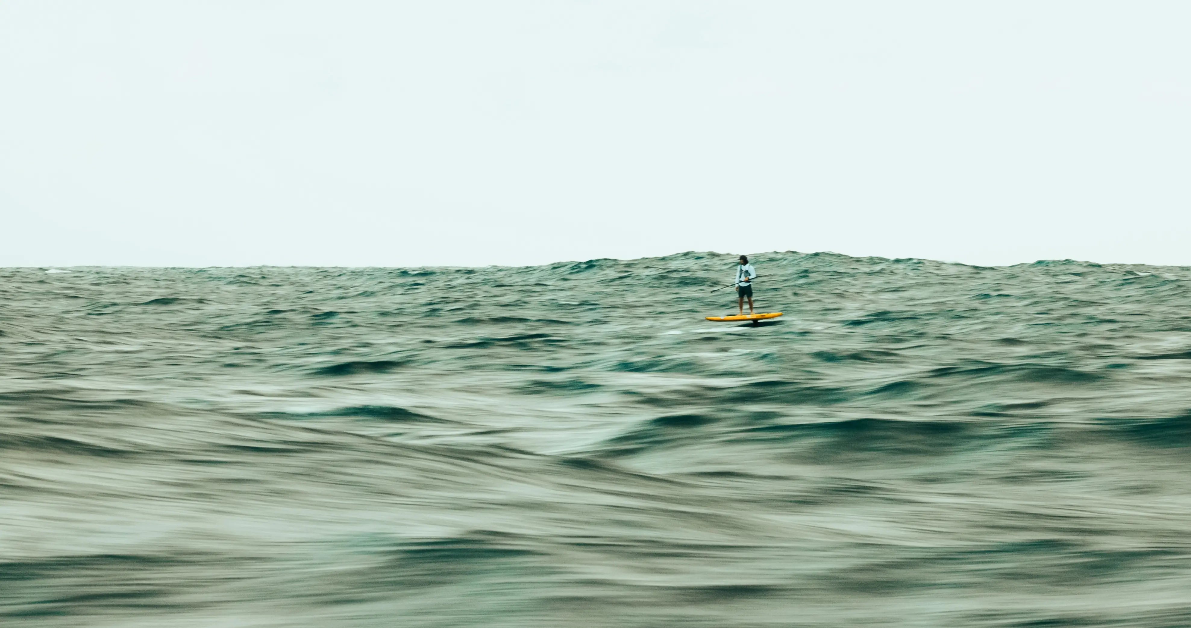 Man riding a downwind foilboard in the ocean with lighthouse in the background