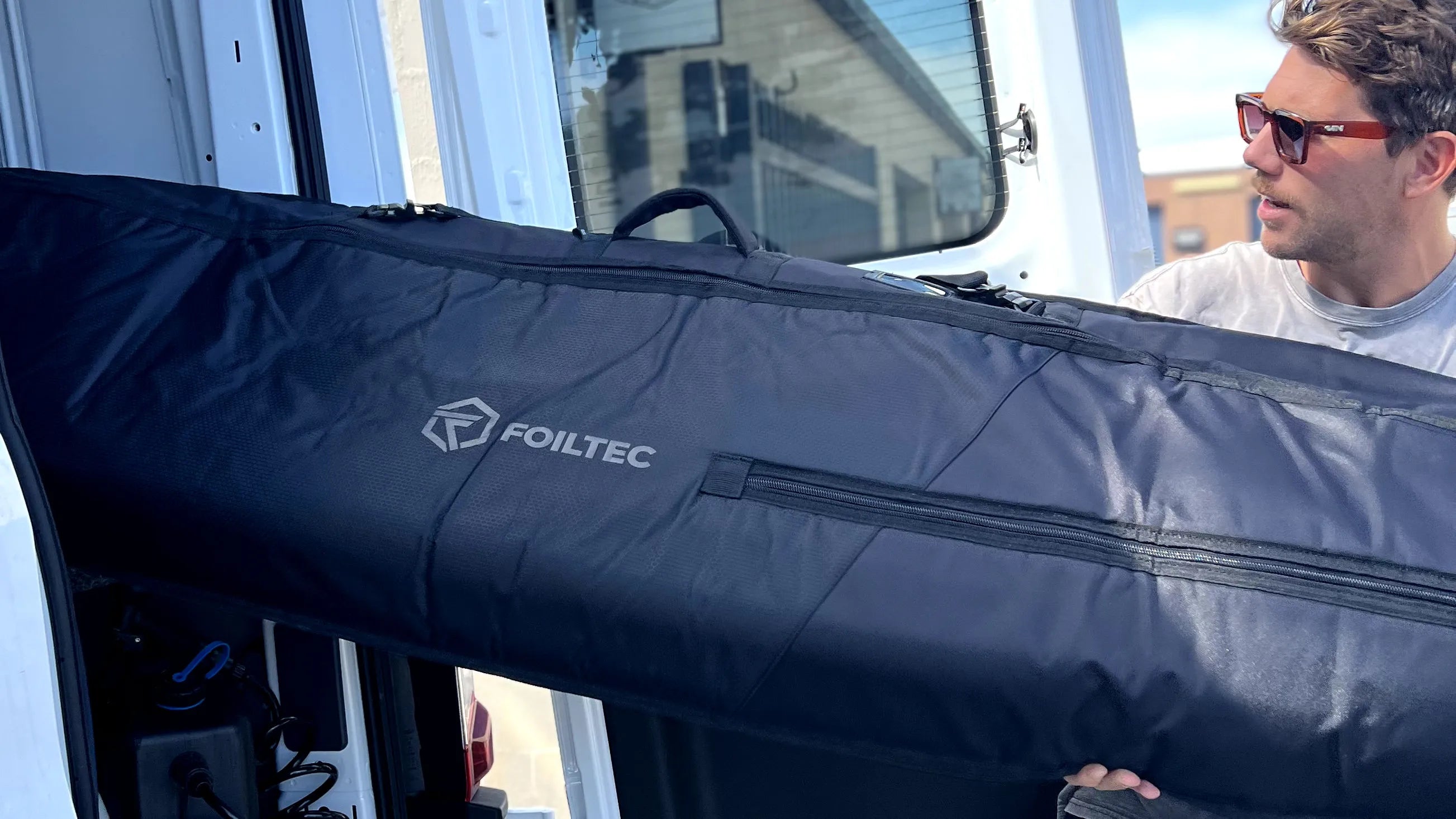 Man putting a downwind hydrofoil board in a foil bag into his white van
