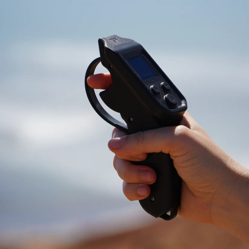 Foil Drive V3 Throttle Controller held in a hand with the beach and ocean in the background.