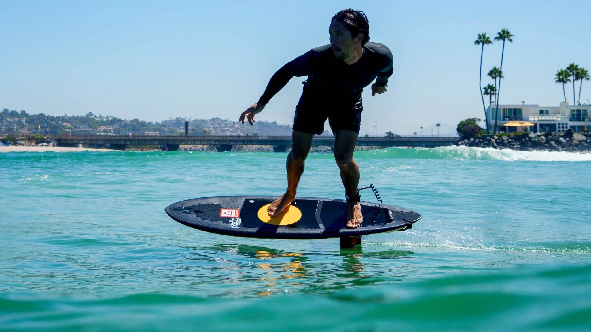 Josh Ku Pro Foilboarder on a foil board called the Kruzer made in Australia by foilboard manufacturer Amos Shapes in the ocean with palm trees and buildings in the background