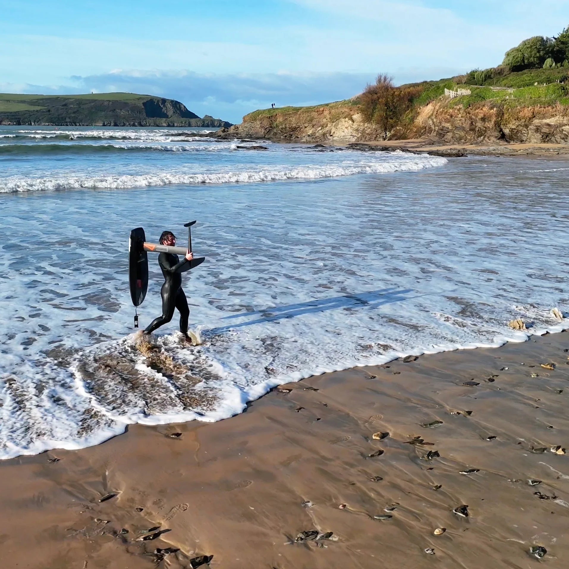 Amos Shapes team rider Tom Earl carrying hydrofoil board the Nano V2 and code foils on a beach